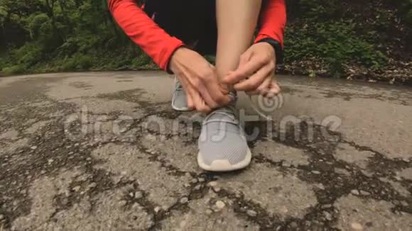 一个年轻的白种人女孩坐在高加索地区的一条森林道路上慢跑之前她把鞋带绑起来广角视频的预览图