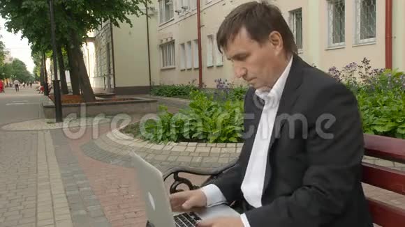 商人在笔记本电脑上打字坐在街上的长凳上视频的预览图