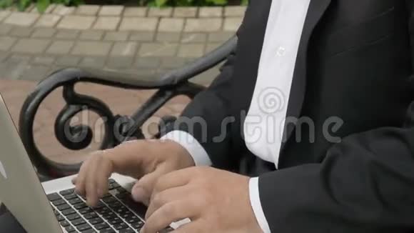 商人在手提电脑上打字坐在街上的长凳上视频的预览图
