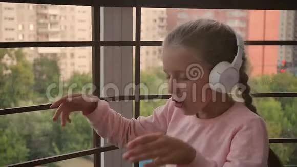 美丽可爱快乐的小女孩在无线耳机上听音乐有趣的小女孩唱着歌视频的预览图