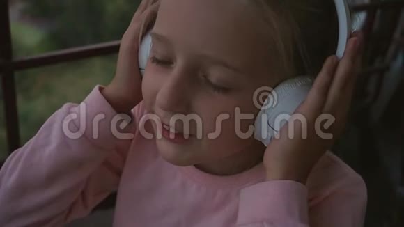 美丽可爱快乐的小女孩在无线耳机上听音乐有趣的小女孩唱着歌视频的预览图