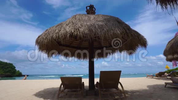 在巴厘岛的天堂海滩上带两个空日光浴床的稻草大伞视频的预览图