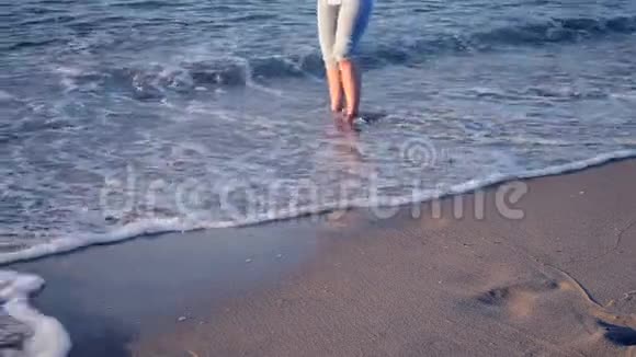 3女孩站在海边早晨她的脚被海浪卷起来视频的预览图