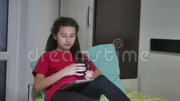 十几岁的女孩正在吃三明治在室内平板电脑上玩一个在线游戏女童社交媒体视频的预览图