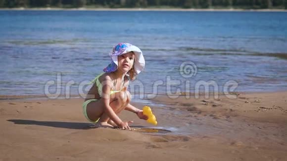 可爱的金发小女孩在湖边玩沙子视频的预览图