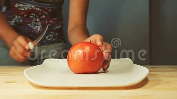 一个年轻的女人在厨房内部的切割板上用刀切割半个新鲜多汁的西红柿视频的预览图
