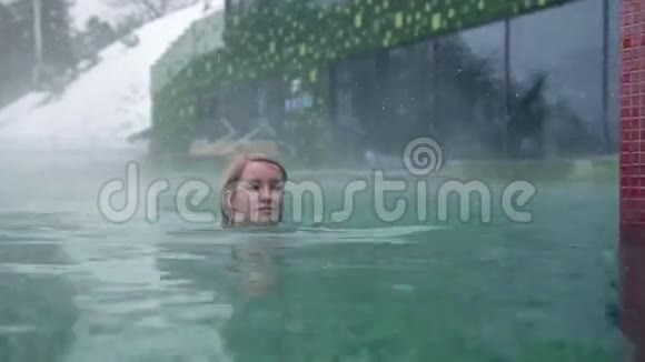 穿着蓝色比基尼的年轻女子在室外游泳池里游过镜头视频的预览图