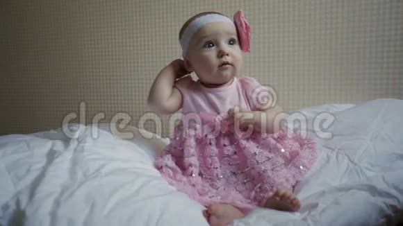 一个穿着粉红色裙子坐在床上的漂亮小女孩视频的预览图