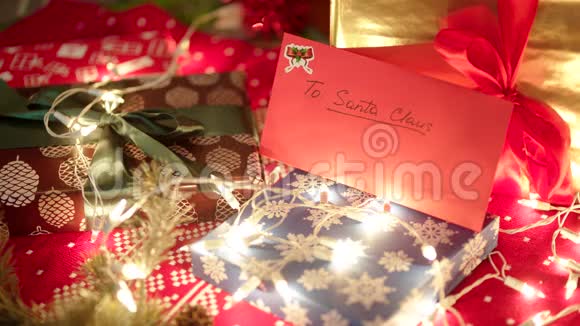 一个红包和致圣诞老人的信躺在圣诞树下的礼盒和明亮的灯光下视频的预览图