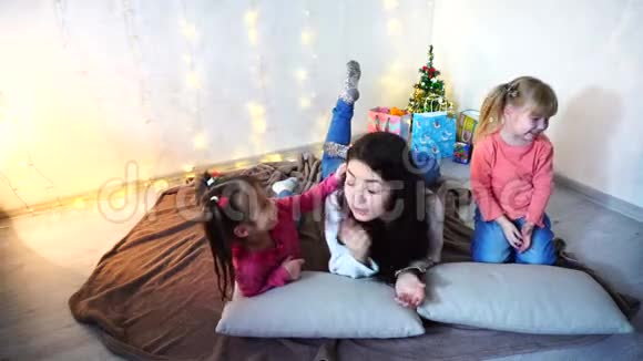 可爱的女性和两个小女孩的孩子摆着相机微笑着躺在垫子上在房间的地板上视频的预览图