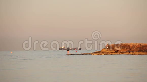 一个渔夫在黎明的海面上捕鱼一个渔夫在黎明的天空下在岩石上捕鱼一群渔夫和一群剪影视频的预览图