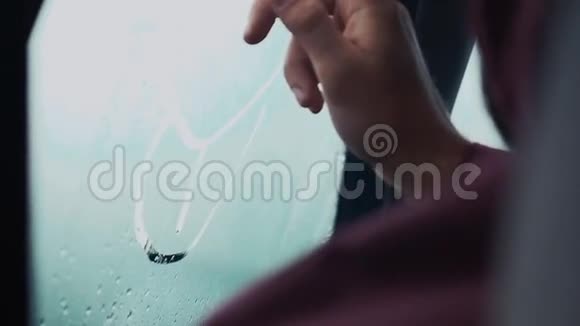 一个人用一根手指在车里的窗户上画画外面下雨的天气空投视频的预览图