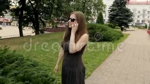 戴墨镜的漂亮女孩在户外散步时用智能手机说话视频的预览图
