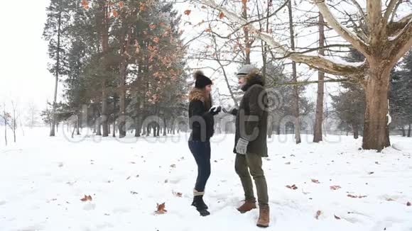一个年轻人和一个穿着温暖冬天衣服的女孩在一个下雪的冬天公园里享受彼此的存在视频的预览图