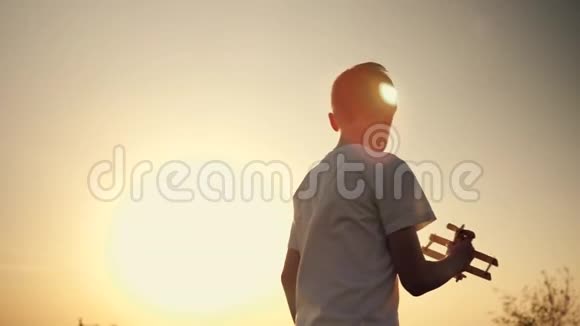 一个孩子正在日落时玩玩具飞机一个男孩拿着玩具的剪影手拿着一架小飞机这就是视频的预览图