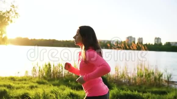 日落时分女人穿过湖岸上的公园慢动作视频的预览图