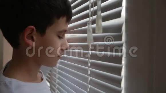 男孩从窗户透过百叶窗看着街道视频的预览图