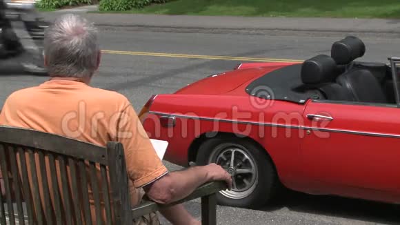 一个男人坐在一辆红色跑车前看着摩托车经过视频的预览图