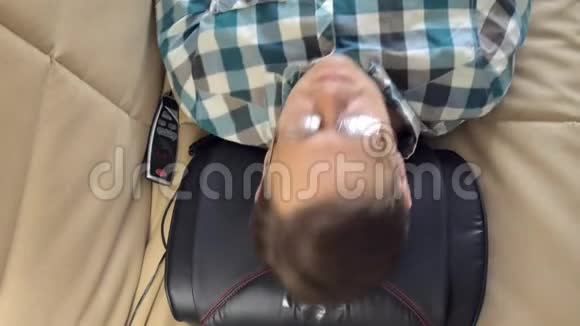 男人躺在家里的沙发上躺在按摩器的头下放松的状态视频的预览图
