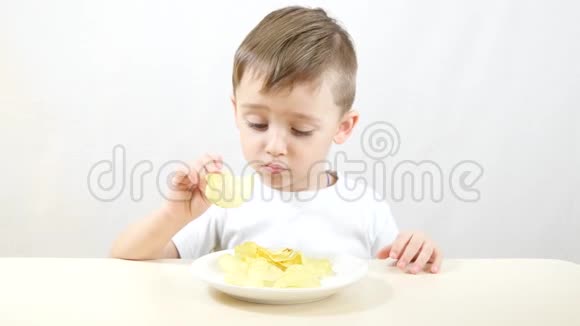 一个喜欢吃薯片的孩子坐在白色背景的桌子旁视频的预览图