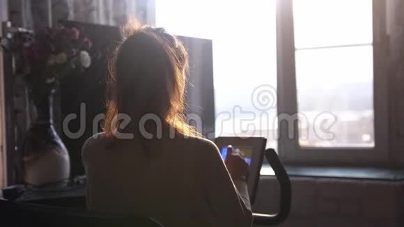 年轻的黑发女人在家靠窗的自行车模拟器上练习在日落时用镜头看城市视频的预览图