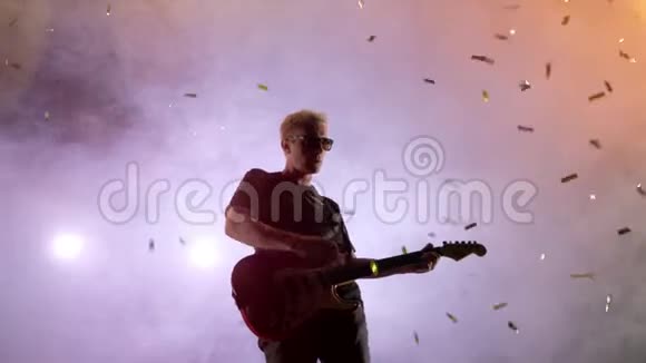 吉他手在舞台上表演舞台灯光烟雾从高处落下的金色纸屑视频的预览图