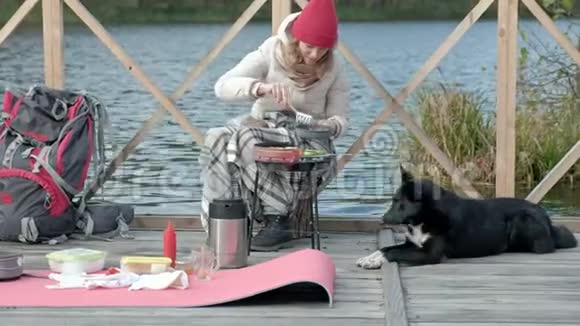 女游客穿着温暖的衣服在河岸附近的桥上背着背包准备烤蔬菜喂饭视频的预览图
