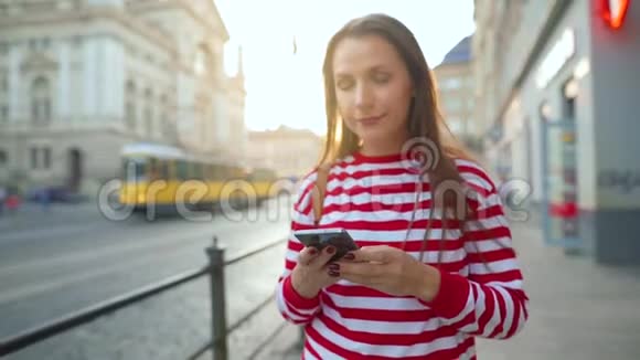 日落时分女人用智能手机走在老街上交流社交网络网上购物概念视频的预览图