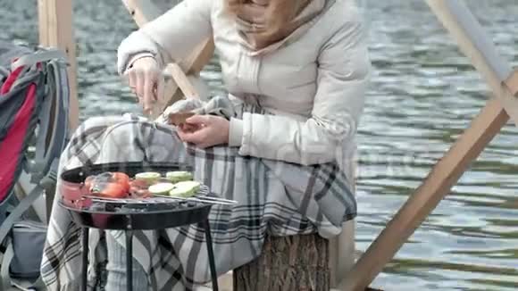 女游客穿着温暖的衣服在河岸边的桥上背着背包准备烤蔬菜喂饭视频的预览图