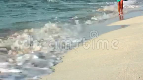 美丽的晒黑的女性双腿在海浪中沿着海岸行走只有双腿在视频中和影子在沙滩上移动视频的预览图
