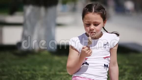 可爱的女孩在夏天的阳光日在公园里吃棕色冰淇淋视频的预览图