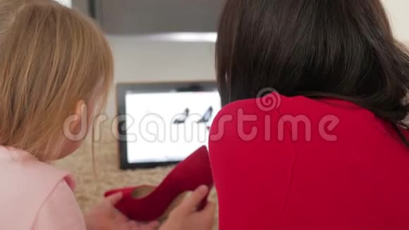 母亲和小女儿在数码平板电脑上网上购物时看鞋类网上购物的概念视频的预览图