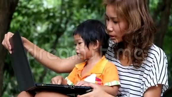 一位亚裔男孩和母亲正在公园里使用笔记本电脑视频的预览图