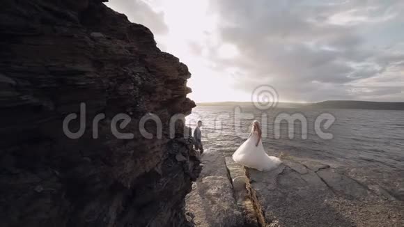 新婚夫妇一起在海边的山坡上可爱的新郎和新娘慢动作视频的预览图