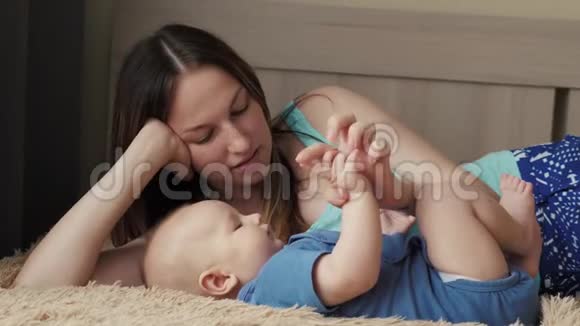 母亲和孩子在一张白色的床上妈妈和小男孩穿着尿布在阳光明媚的卧室里玩家长和小孩放松视频的预览图