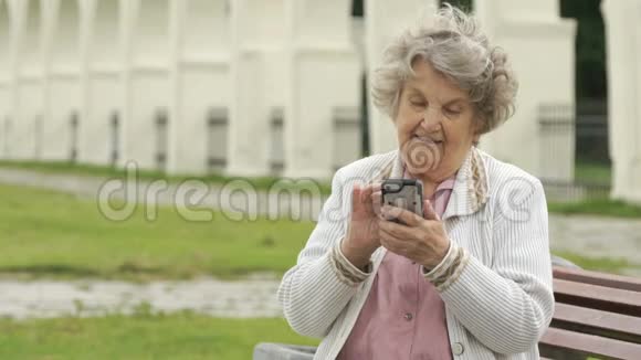 成熟的老妇人在户外手持银色智能手机视频的预览图