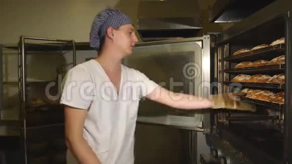英俊的面包师穿着统一的托盘装满了新烘焙的面包在制造业视频的预览图