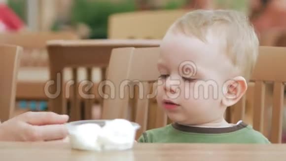 妈妈用勺子喂小儿子吃冰淇淋他们坐在一家街头咖啡馆里这个男孩真的很喜欢视频的预览图