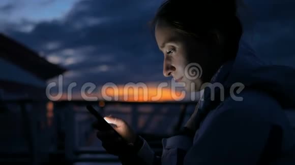 晚上在游轮甲板上使用垂直智能手机的女人视频的预览图