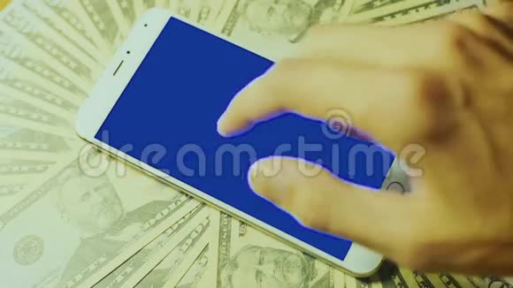 男性手触摸白色智能手机在一堆钞票上显示蓝色钥匙视频的预览图