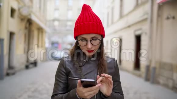 红唇的女人使用智能手机漫步在中世纪的街道上视频的预览图