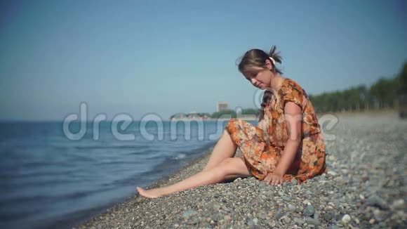 可爱的女孩坐在岸上把鹅卵石扔进海里视频的预览图