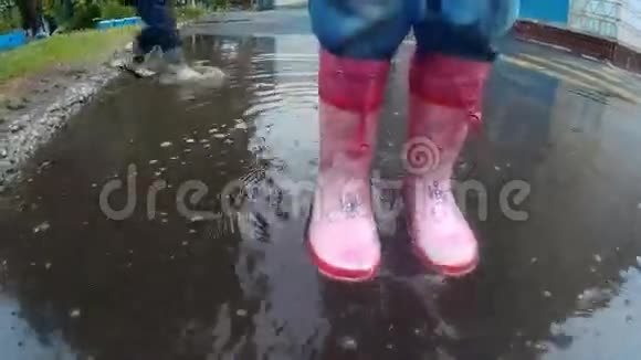 雨后穿靴子的孩子在泥泞的水坑里散步和跳跃视频的预览图