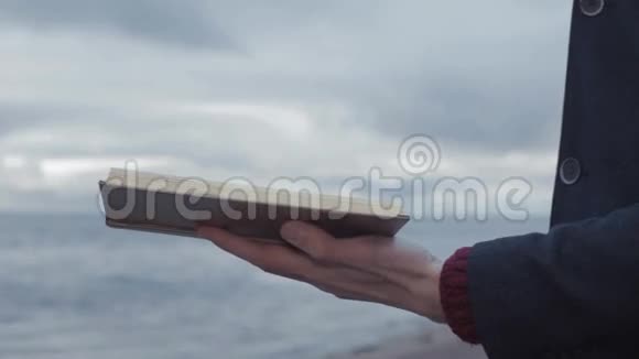 年轻男子点燃手中的书站在海岸风暴云的背景上视频的预览图