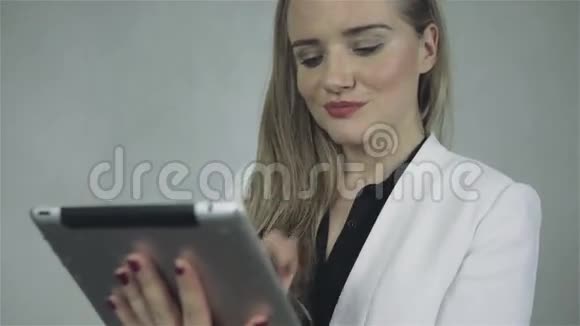 年轻优雅的女人站在灰色背景和触摸板上的肖像视频的预览图