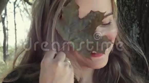 手握秋叶秋叶背景的年轻女子视频的预览图