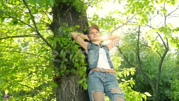 美丽的女孩穿着牛仔裤的衣服在日落时在森林里的树上摆姿势视频的预览图