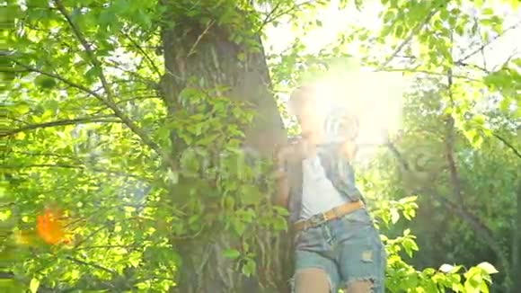 美丽的女孩穿着牛仔裤的衣服在日落时在森林里的树上摆姿势视频的预览图