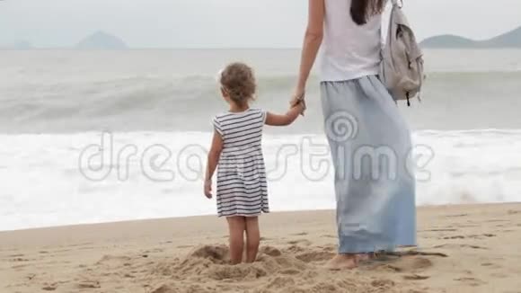 母亲和小女儿在恶劣的天气下沿着大海散步视频的预览图