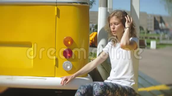 年轻女子在户外乘坐黄色马车用智能手机听耳机音乐放松享受概念视频的预览图